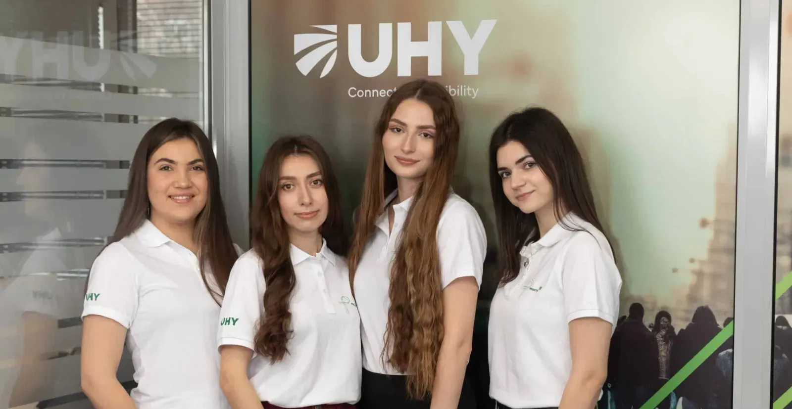 Четыре сотрудницы UHY Prostir в фирменных поло на фоне баннера UHY