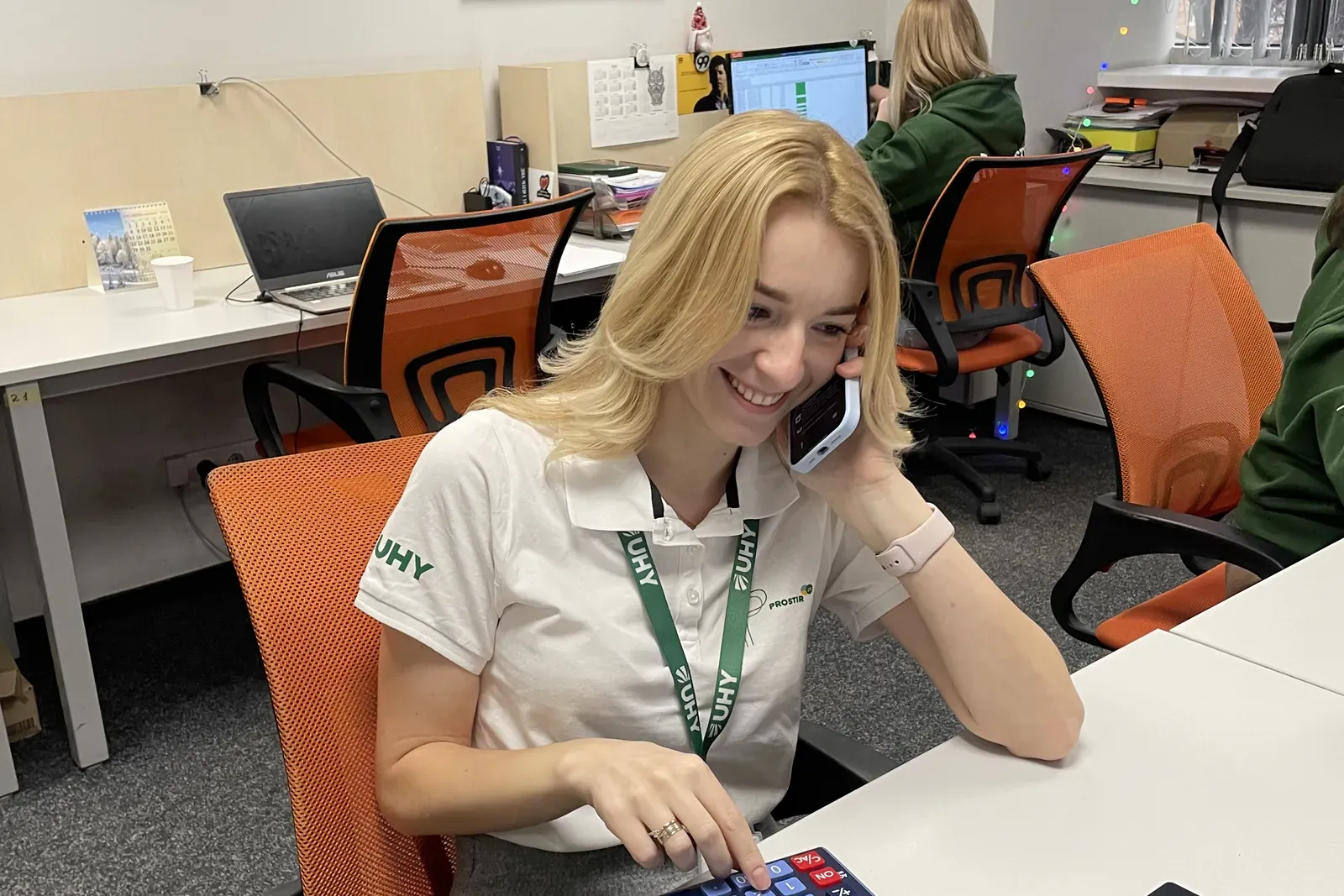 Сотрудница UHY Prostir в фирменном поло разговаривает по телефону и считает на калькуляторе