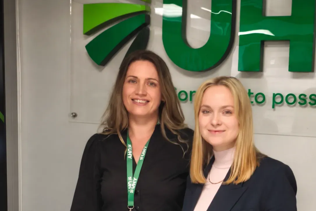 Две сотрудницы UHY Prostir на фоне логотипа UHY в офисе